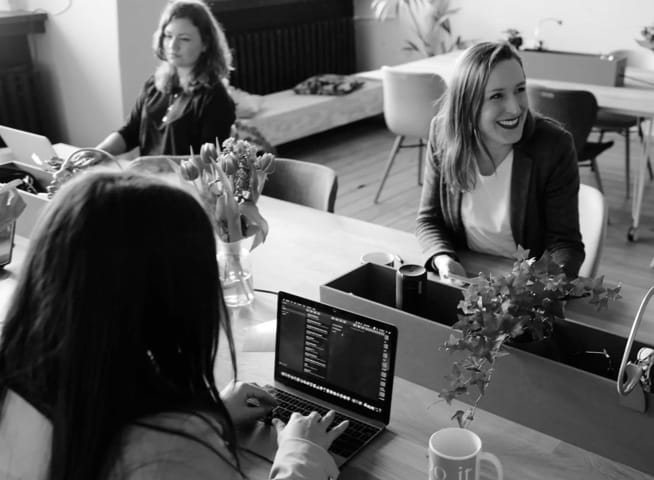 Three colleagues working on laptops around a shared office table.